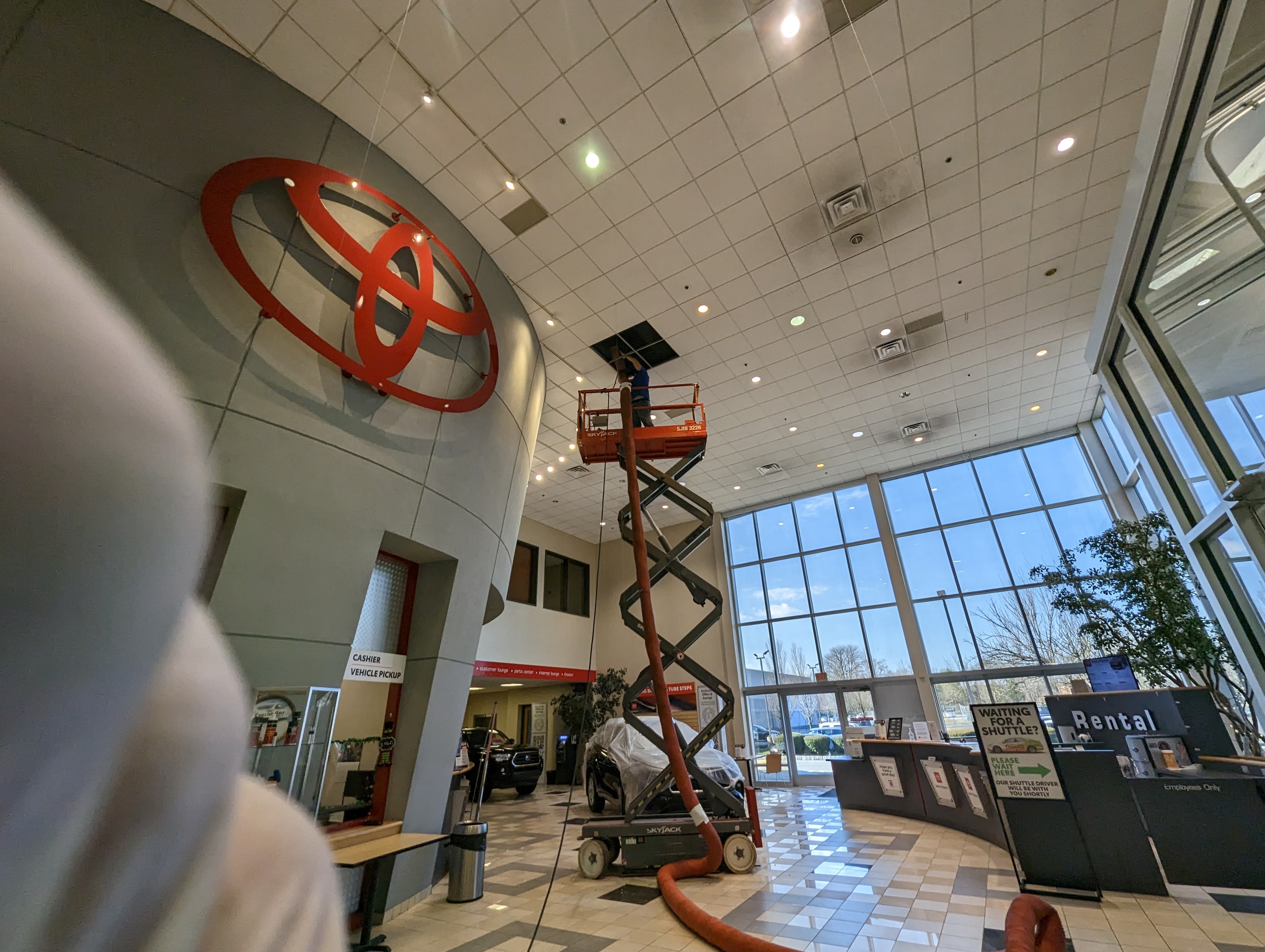 Technician on scissor lift cleaning high-ceiling ductwork inside Toyota dealership